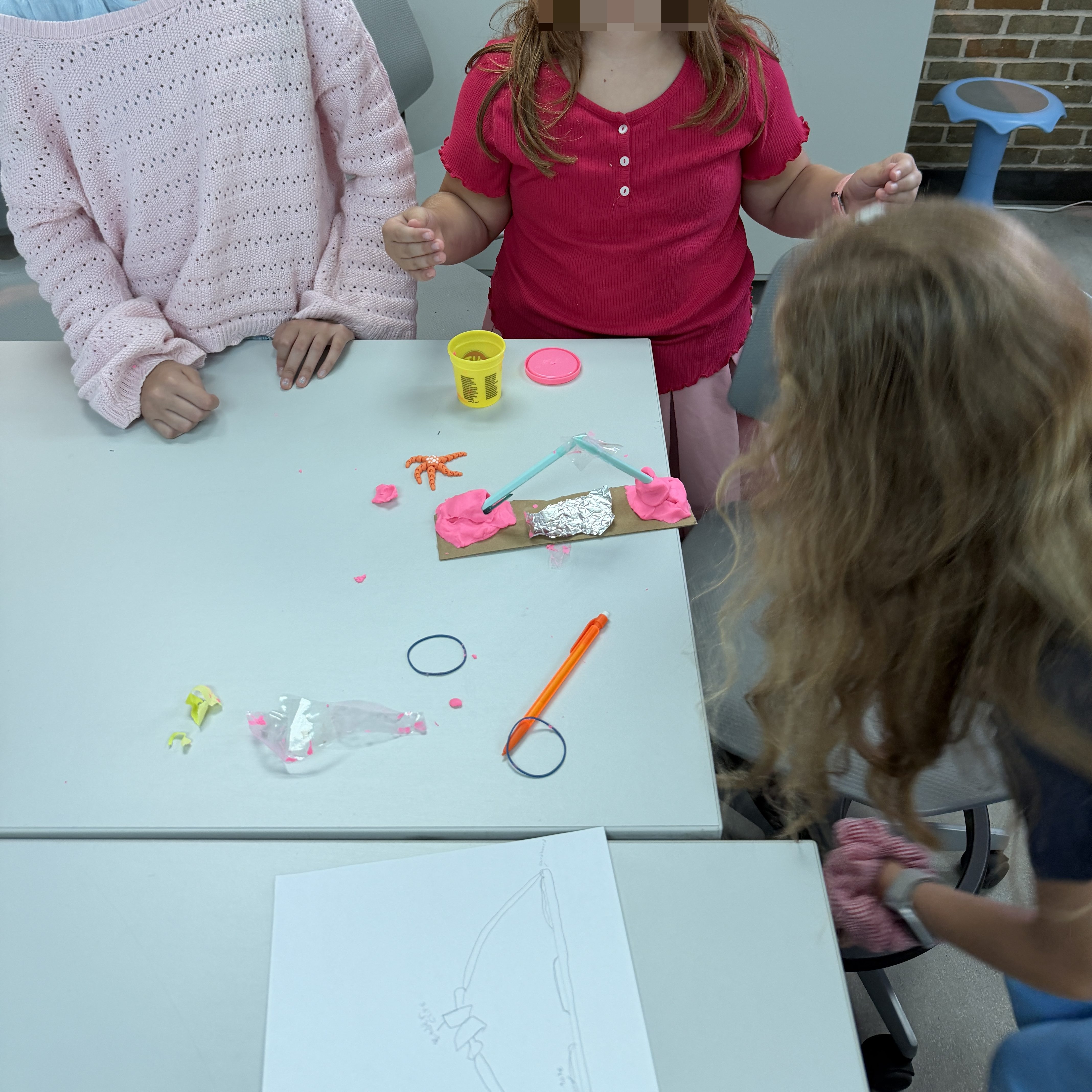 Students gather around a table during a Makey Makey conductivity investigation, testing everyday materials such as foil, cardboard, and Play-Doh to see which ones conduct electricity.